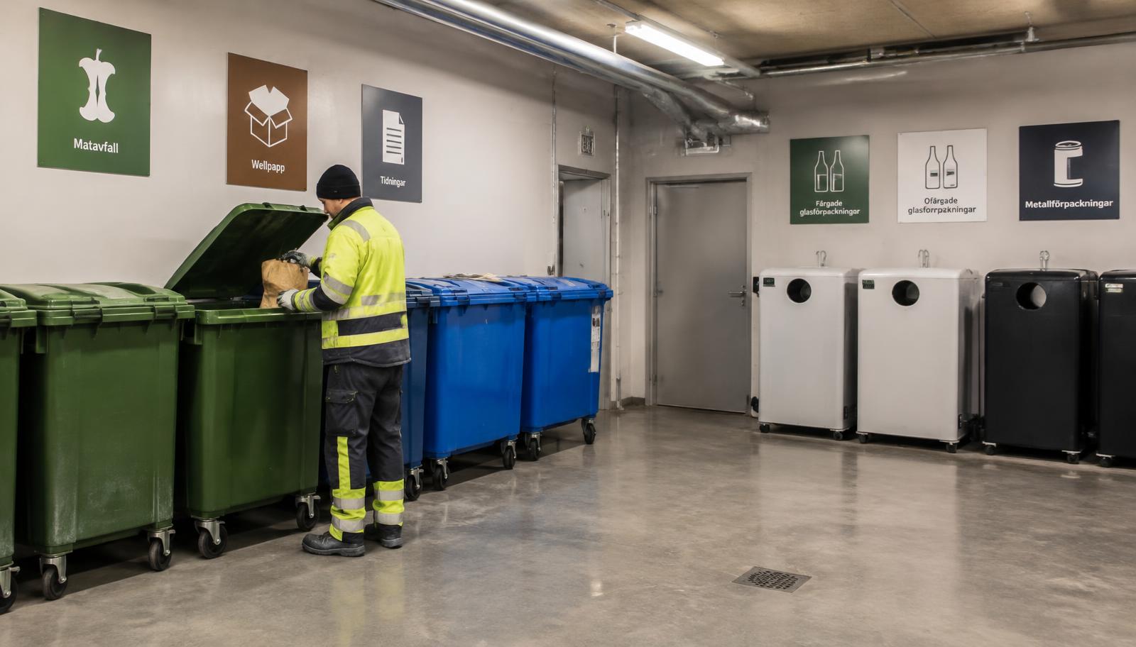 Återvinningsrum med sorterade kärl, skyltning och personal i varselkläder
